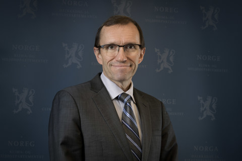 Utenriksminister Espen Barth Eide smilende i mørk dress med blå bakgrunn