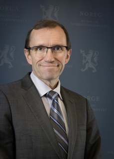 Utenriksminister Espen Barth Eide smilende i dress med blå bakgrunn 