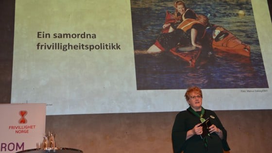 Kulturministeren på scenen med powerpoint på storskjerm om frivilligheitsmeldinga bak seg.