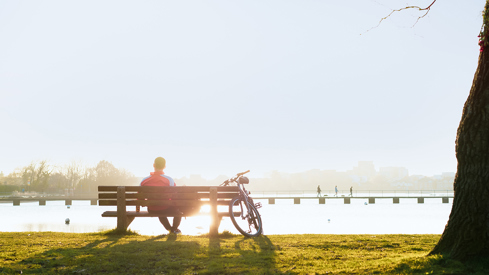 Man sitting with his back to the camera on a bench, bike to his side, water in front