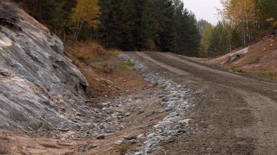 Ny ombygd skogsbilvei i 2015. Byggeteknikk med bærelag av grovknust fjell. Slitelag med knust maskingrus. Denne byggeteknikken gir meget solide veier med helårs bæreevne uavhengig av tele og nedbør. Bildet er tatt før siste del av slitelaget er lagt ut. 