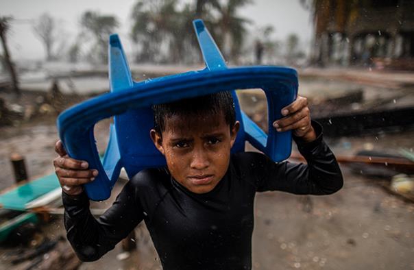 Et barn i Bilwi, Nicaragua beskytter seg mot regnet med en plaststol. Han står på samme sted som der huset hans pleide å
være, etter at det ble ødelagt av orkanen Iota.