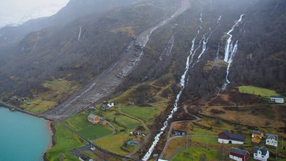 Biletet viser ei fjellside der det er gått eit stort ras. På biletet ser ein at raset har sperra av ein veg som går inn til bustader.