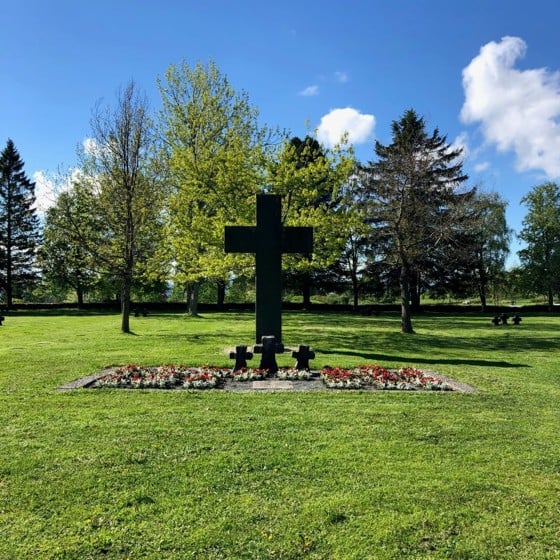 Tysk krigsgravplass på Havstein gård på Byåsen. Et stort steinkors med tre små steinkors og blomster foran.