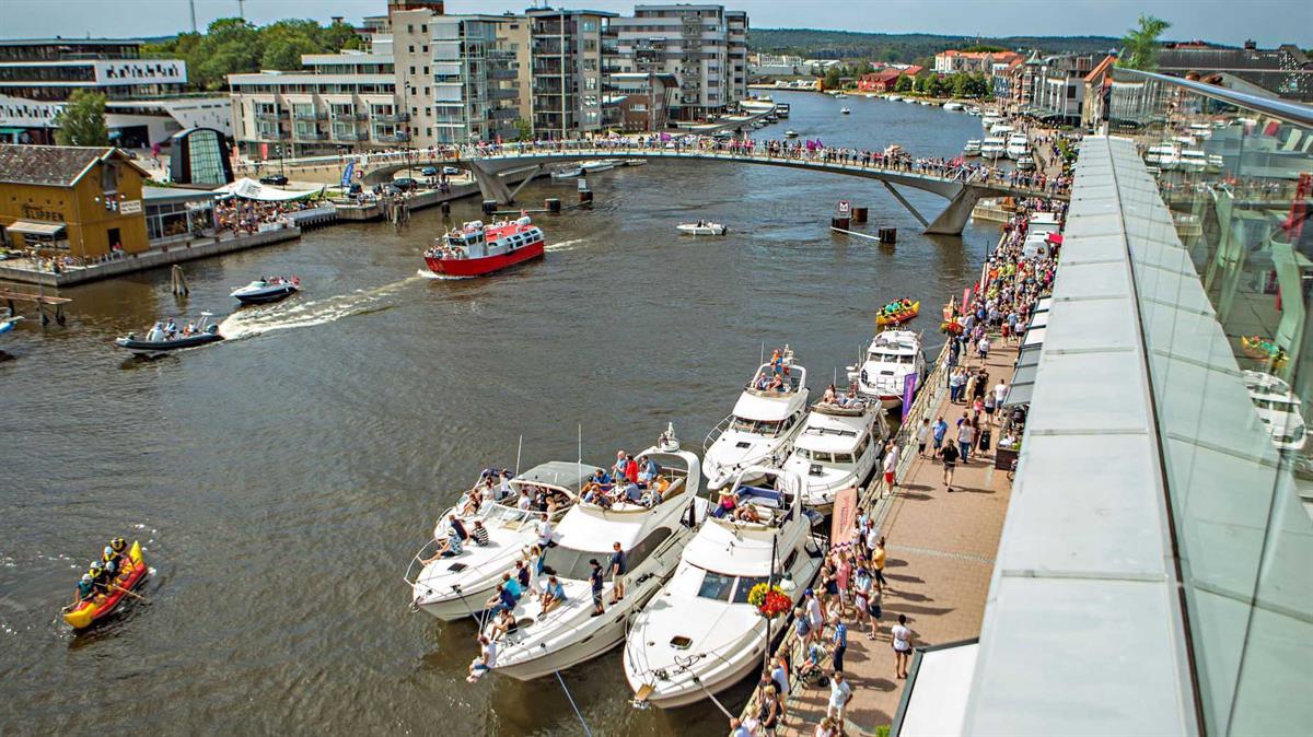 Oversiktsbilde som viser begge sider av Glåma med byferge, fritidsbåter og folk på kaien.