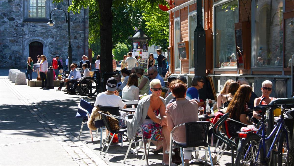 Sommer i Midtbyen, folk sitter ved utendørs kafébord i gate.