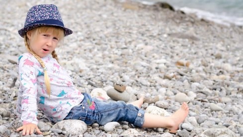 Jente med sommerhatt og shorts sitter på steinstrand