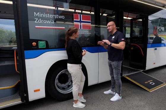 Næringsminister Cecilie Myrseth besøker Medevac i Polen og får en orientering av en lokalt ansatt. Her foran bussen som Norge har donert.