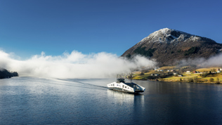 Ferje på en fjord med fjell i bakgrunnen