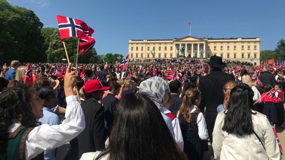 17. maitog på Karl Johan, med folk og flagg i forbrunnen og slottet i bakgrunnen.