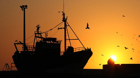 Ein fiskebåt i silhuett mot ein oransje himmel