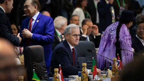 Statsminister Støre sitter ved møtebordet i G20-salen i Rio de Janeiro. Noen sitter, andre står, rundt ham.