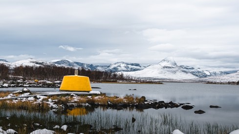 Bilde av et gult grensemerke i betong med snødekte fjell i bakgrunnen.