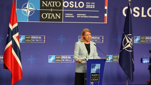 Picture of Foreign Minister Anniken Huitfeldt's at press conference with blue backround and norwegian and NATO flags