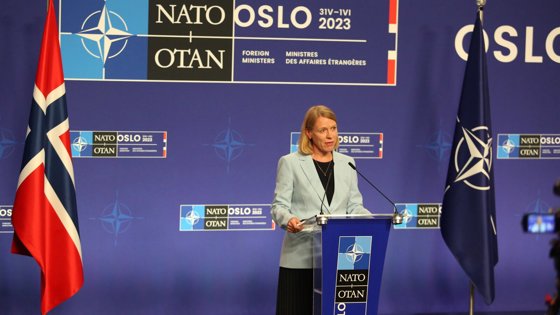 Picture of Foreign Minister Anniken Huitfeldt's at press conference with blue backround and norwegian and NATO flags