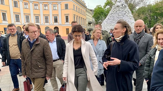 Bilde av ministrene utendørs med monument av sandsekker i bakgrunnen